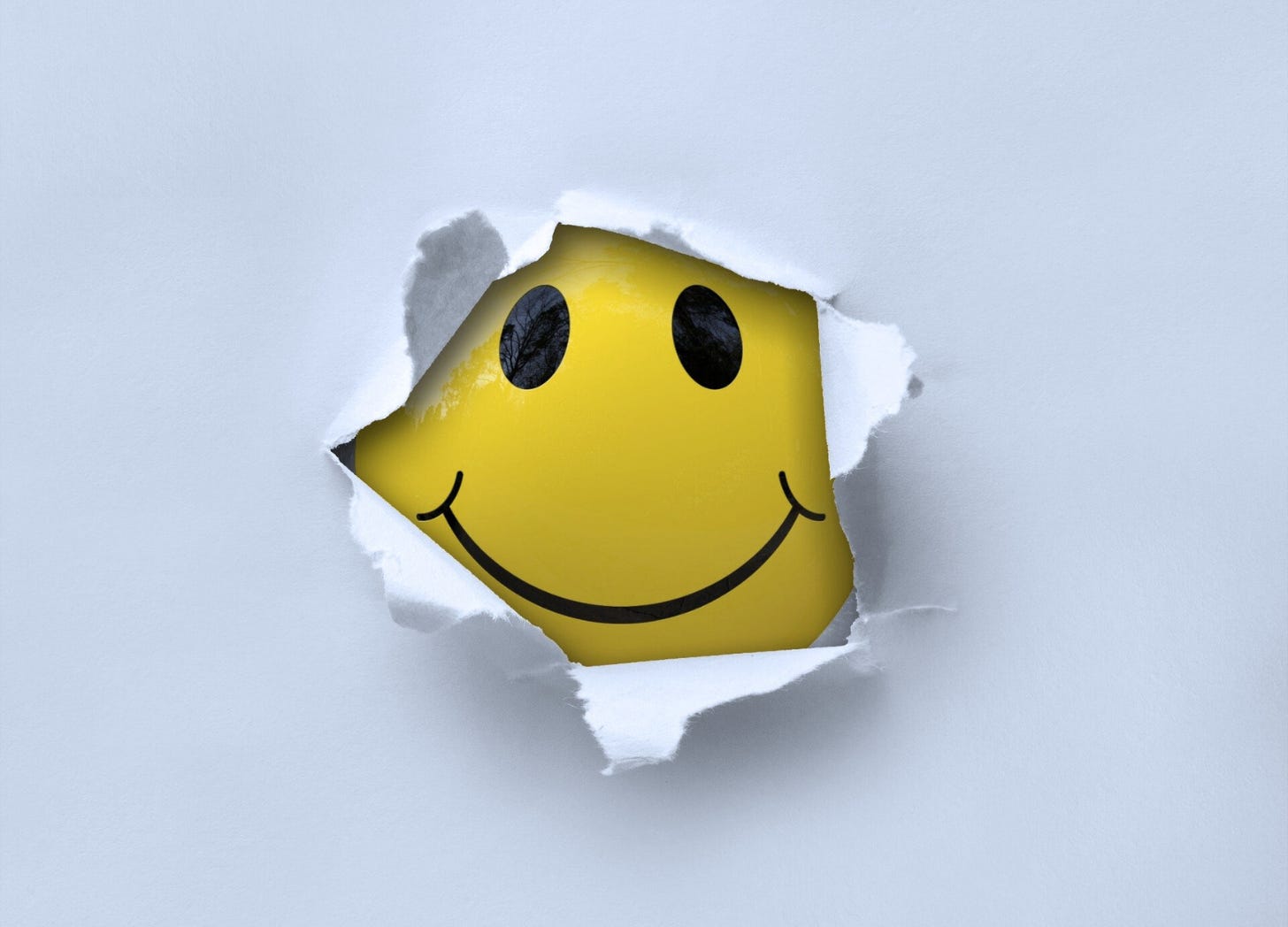 A smiley face emoji breaking through a tear in a blue-gray sheet of paper