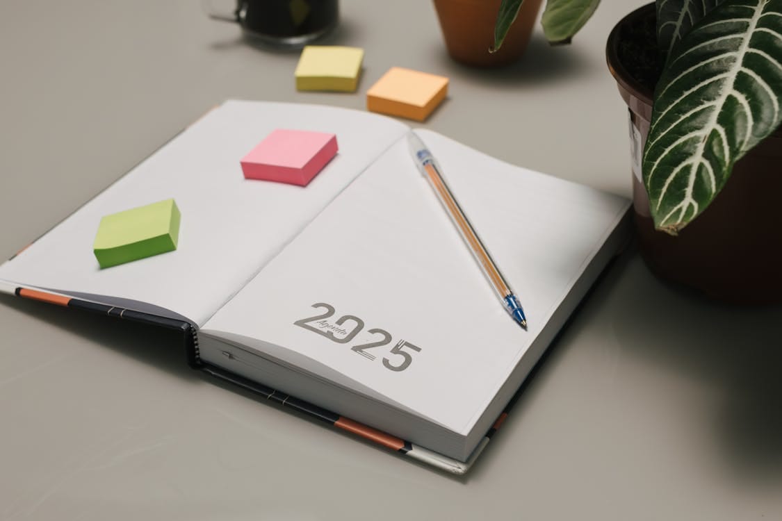 Free Open planner for 2025 with colorful sticky notes and plants on a desk. Stock Photo