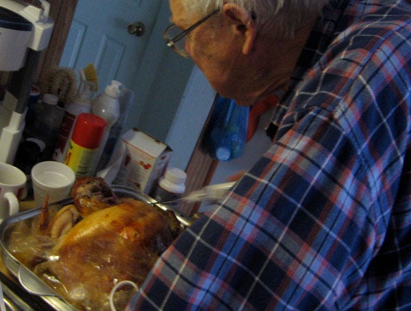 An old white man in a flannel shirt carves a turkey