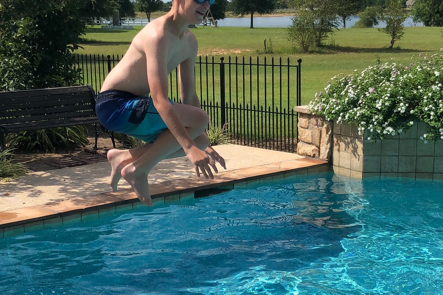 A boy in mid-air as he jumps into the swimming pool