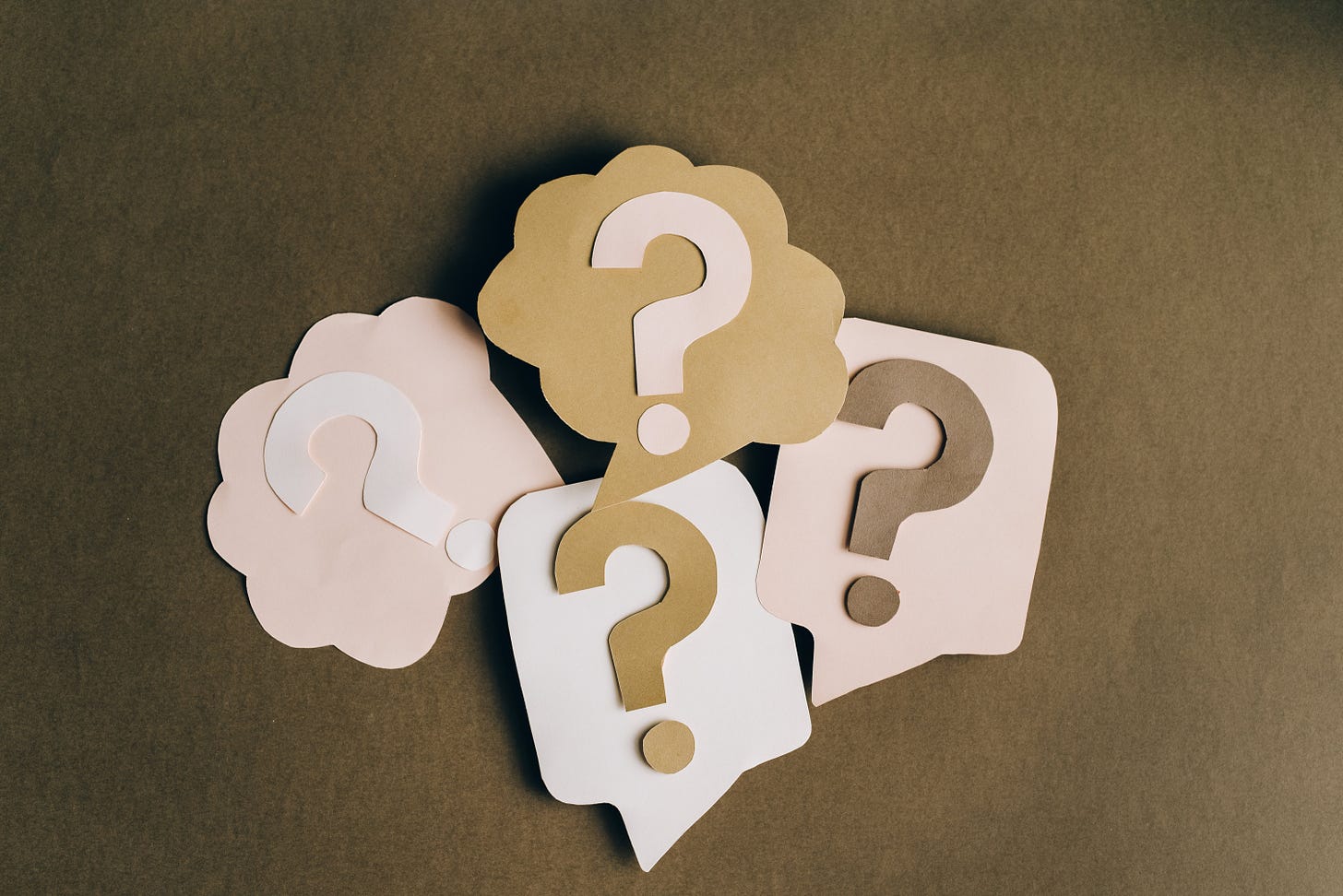 4 paper question mark cutouts in thought boxes that are also cut out, on a brown background. 