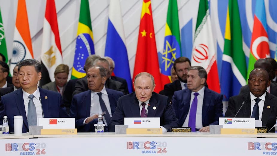 Men seated at a desk with national flags behind them