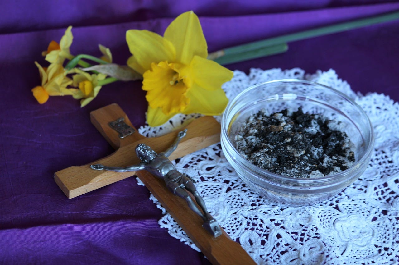 Crucifix of Jesus Christ lays on alter with purple cloth, daffodils, and bowl of ashes for Ash Wednesday during lent.
