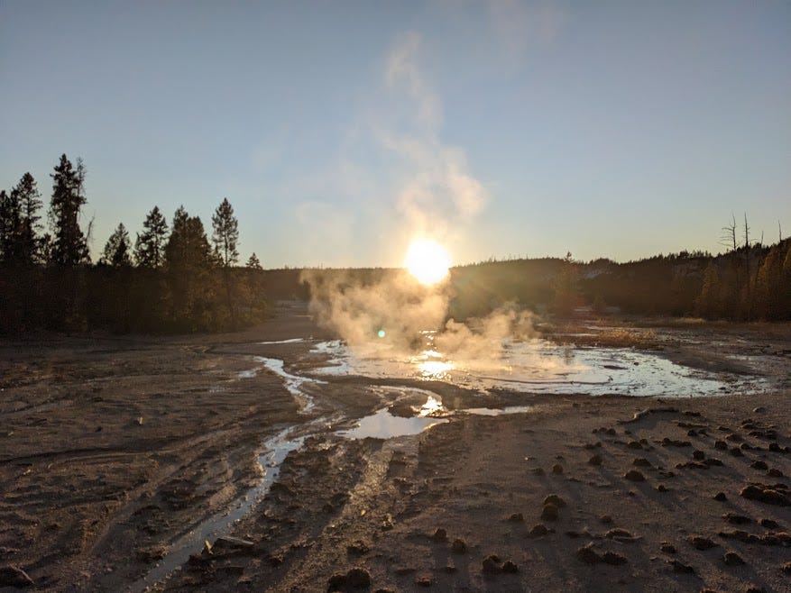 the sun sets in yellowstone over a geothermal happening