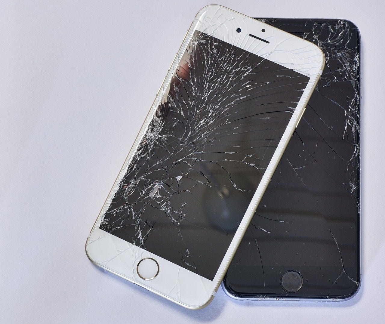 Two iPhones, one black and one white, with cracked screens