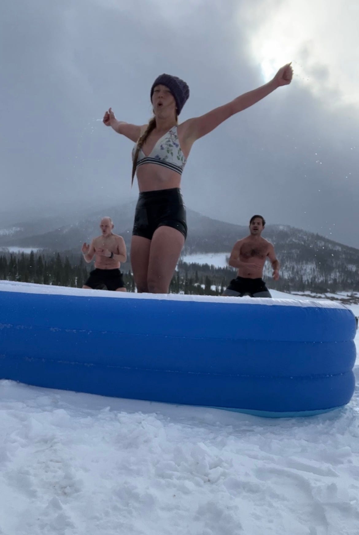 Lisa coming out of ice bath, mountains in background, men doing exercises to keep themselves warm in background