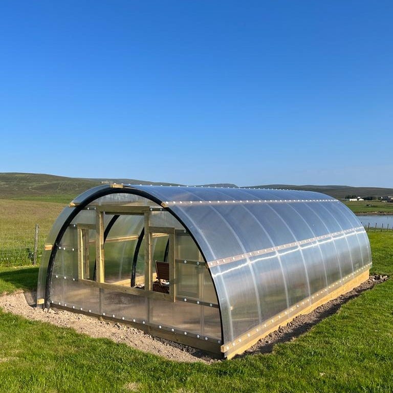 Doug the Crub - the polycrub against the backdrop of green grass, blue skies & the sea