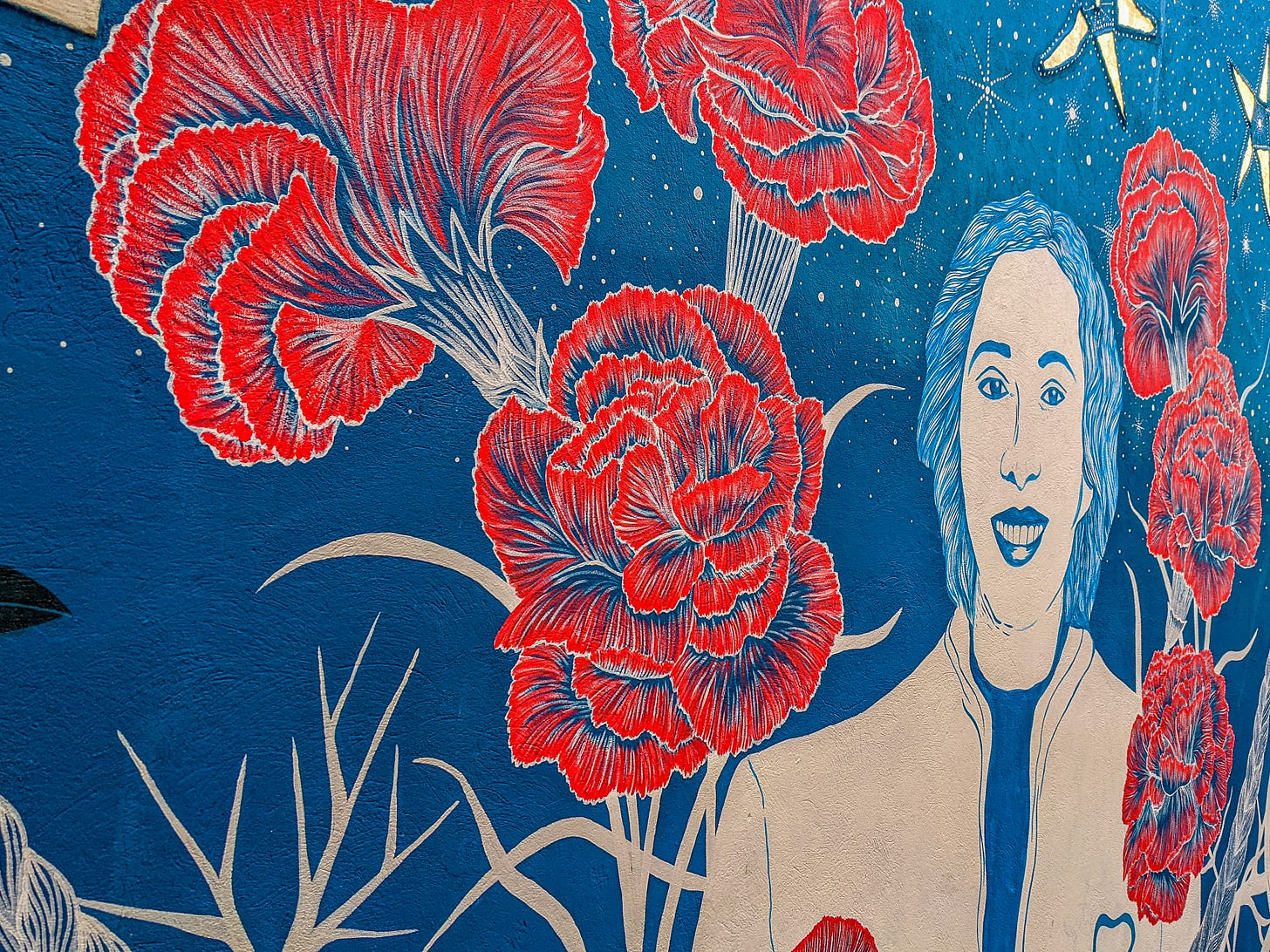 A mural showing a smiling woman in front of blue background filled with red flowers. 