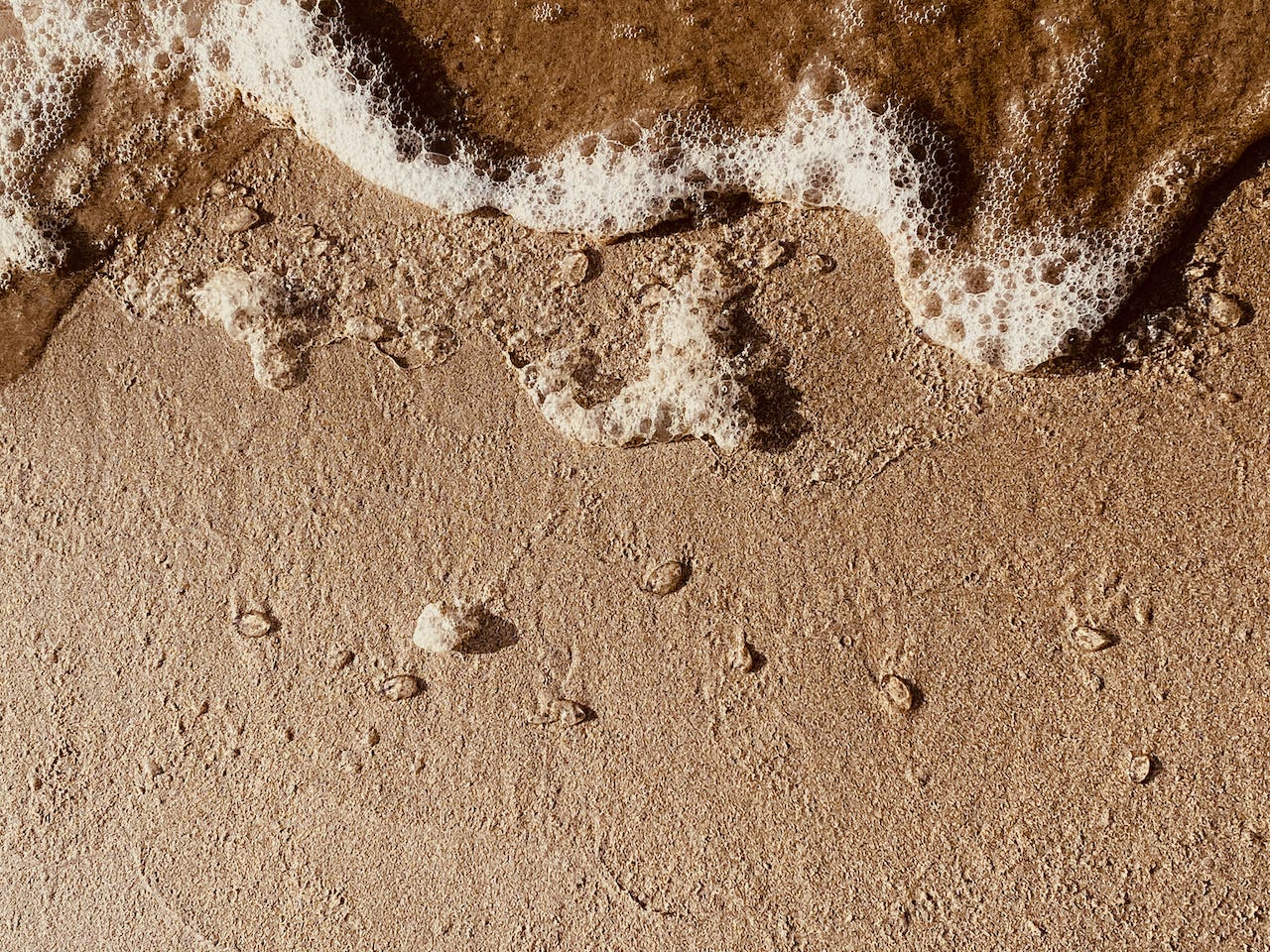 Close up of beach sand, foamy water encroaching from top of frame.