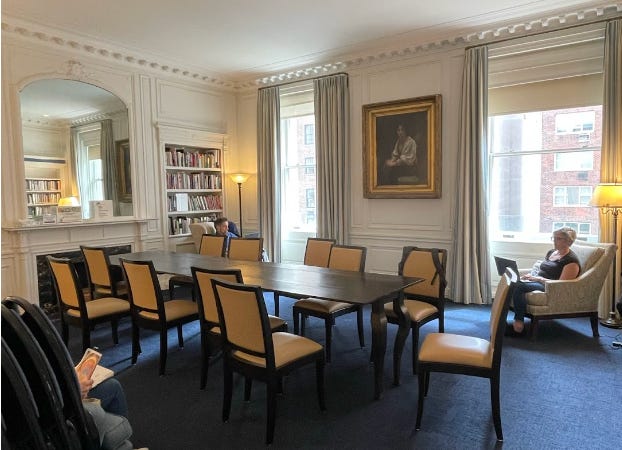 A grand room with two large window, a fireplace and a large central table. The Whitridge Room.