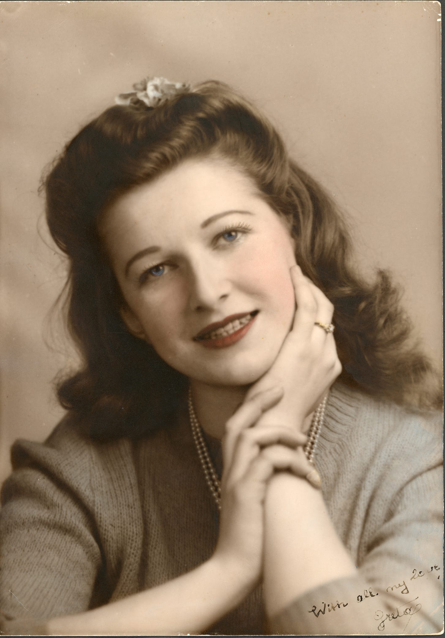 A beautiful young woman wearing an engagement ring looks into the camera with her chin on her hand.