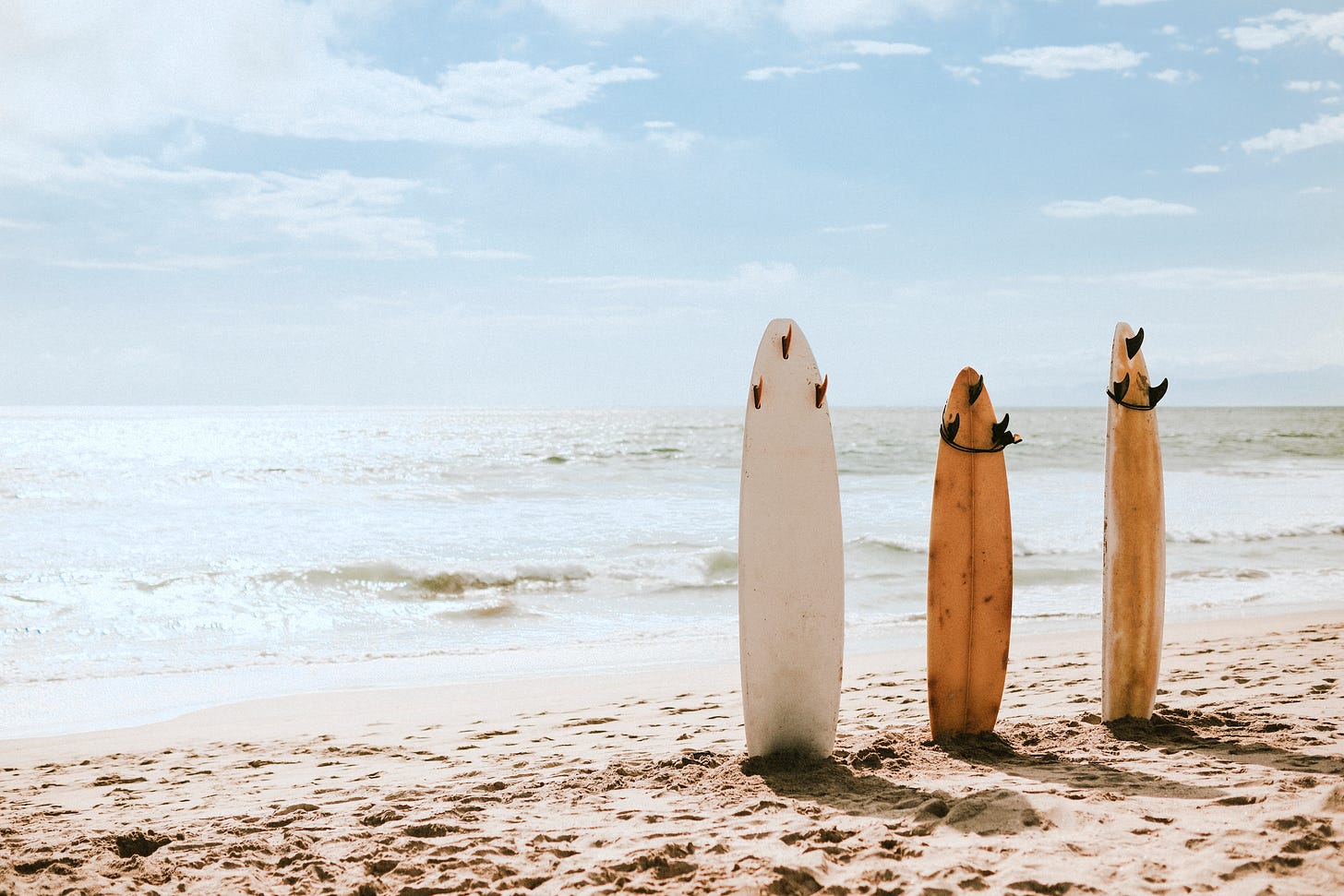 3 surfboards sticking up out of the sand on a beach