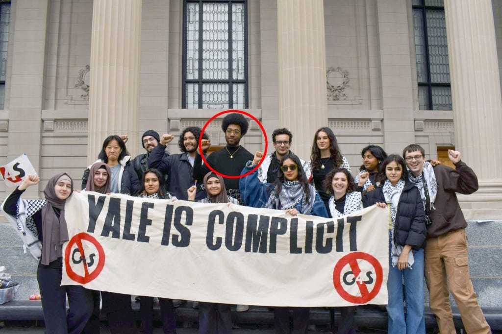 A  group of people standing behind a "Yale is Complicit" banner on the steps of a classical building. 
