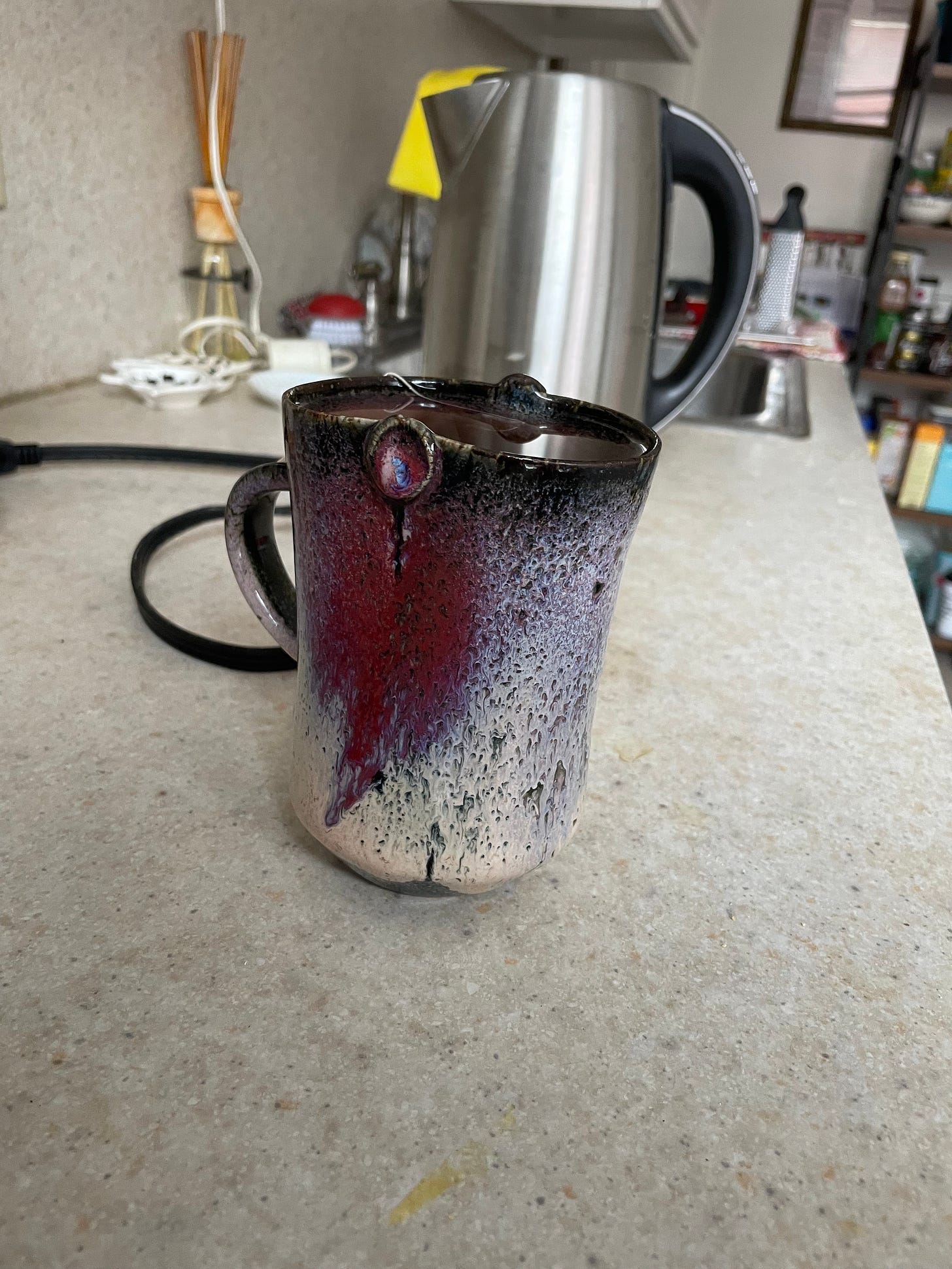 A purple mug with tea in it sits on a kitchen counter, with the kettle and sink visible in the background.