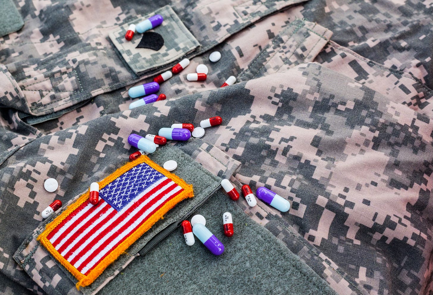 A variety of pills spilled across an ACU blouse with a specialist rank insignia and American flag on it