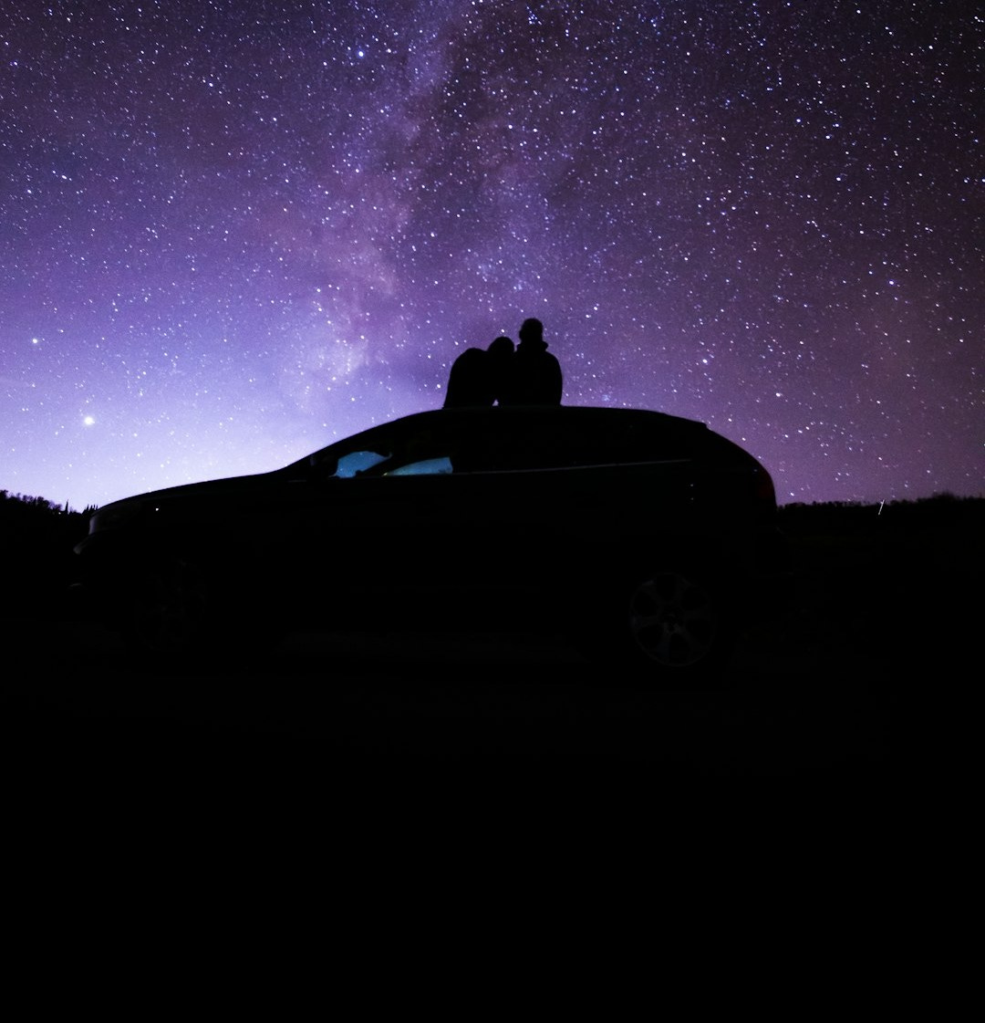 silhouette of person sitting on car under starry night