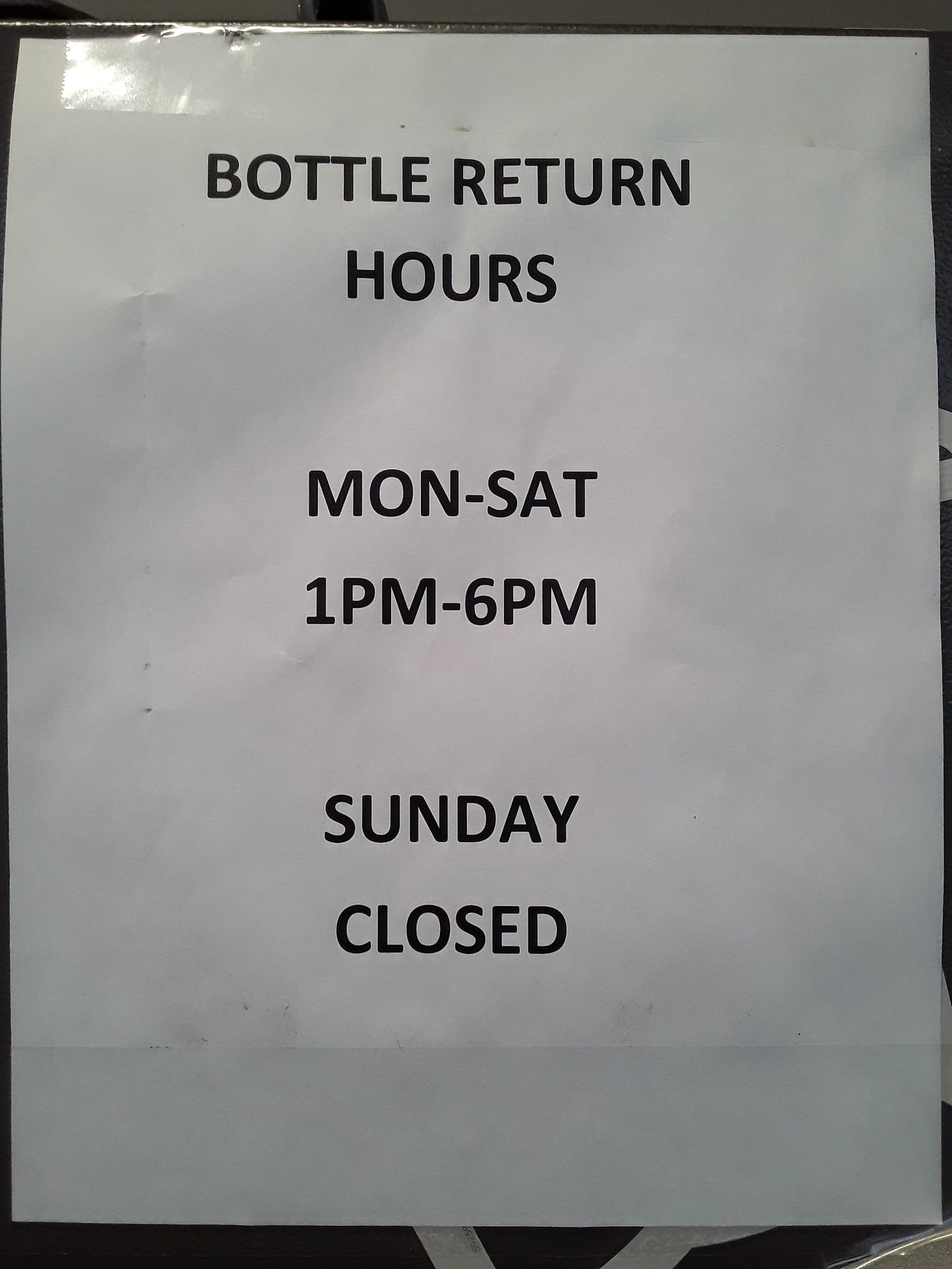 Black and white paper sign taped to a bottle return machine at Midtown Fresh Market in Kalamazoo, Michigan on Saturday, February 10, 2024.  It reads:  "BOTTLE RETURN HOURS, MONDAY THROUGH SATURDAY, 1 P.M. TO 6 P.M., SUNDAY CLOSED".