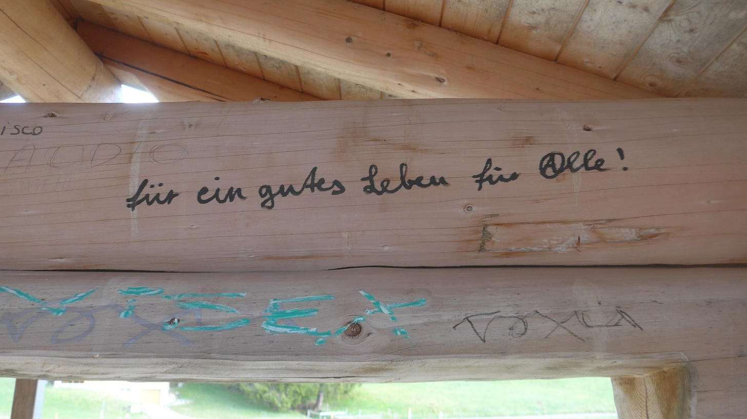 A wooden beam with a graffiti that reads: für ein gutes Leben für (A)lle - the a is a circle A