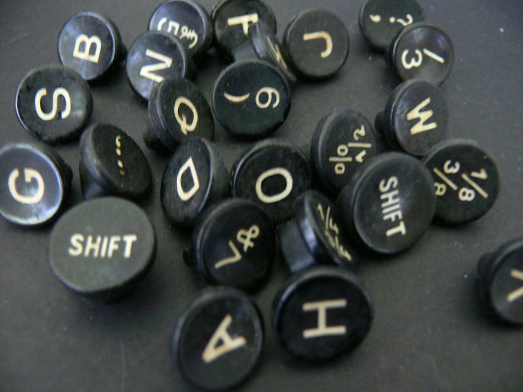 about 25 round keys from a typewriter (with letters, numbers, and punctuation on them) that have been removed from the typewriter and are lying randomly on a black surface about 25 round keys from a typewriter (with letters, numbers, and punctuation on them) that have been removed from the typewriter and are lying randomly on a black surface