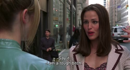 This may contain: a woman standing in front of a man on the street talking to another woman who is holding her hand out