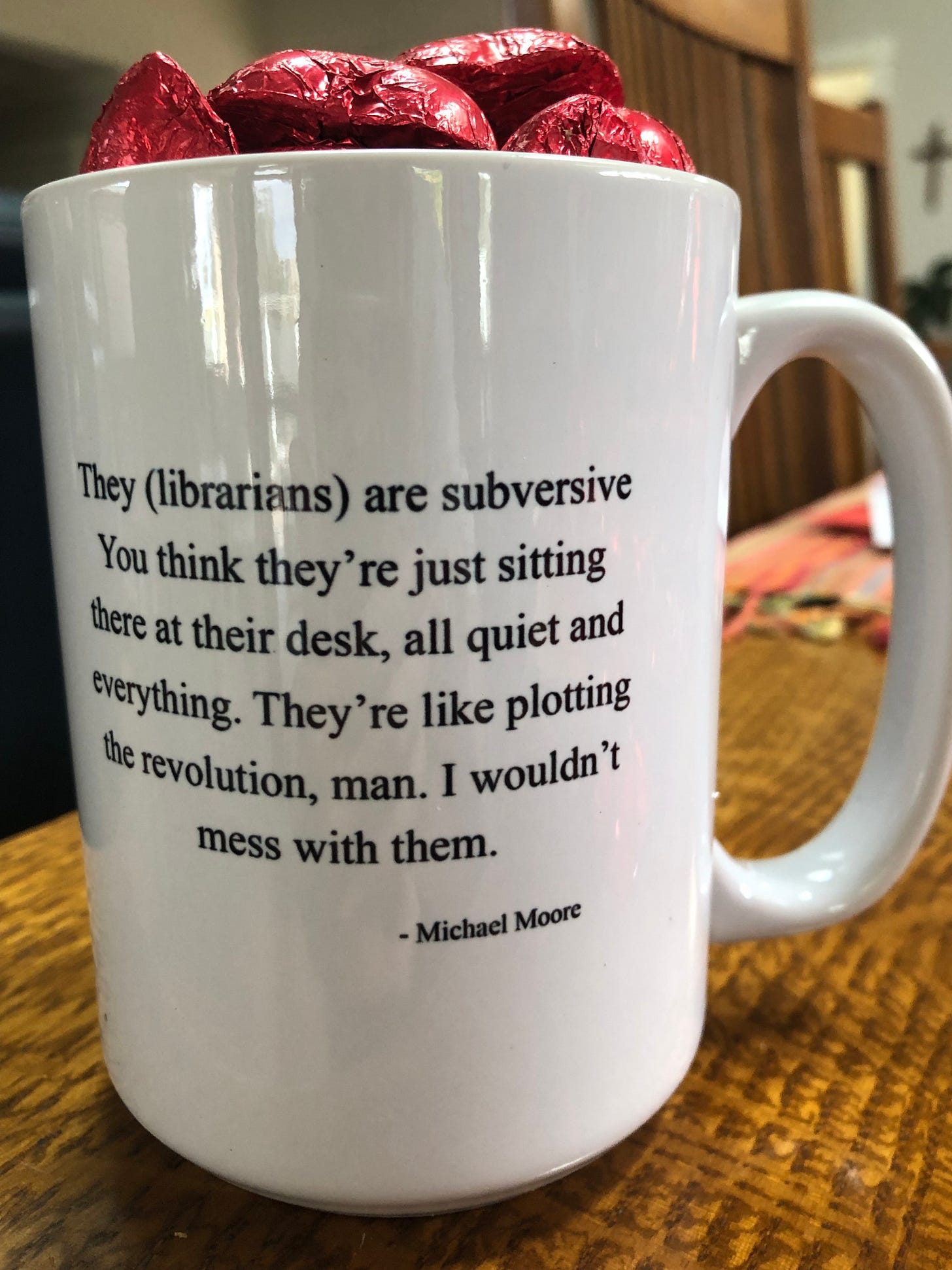 Coffee mug that has these words printed on it: They (librarians) are  subversive. You think they’re just sitting there at their desk, all quiet and everything. They’re like plotting the revolution, man. I wouldn’t mess with them. —Michael Moore