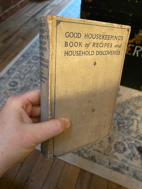 hand holding a worn edition of Good Housekeeping's Book of Recipes and Household Discoveries
