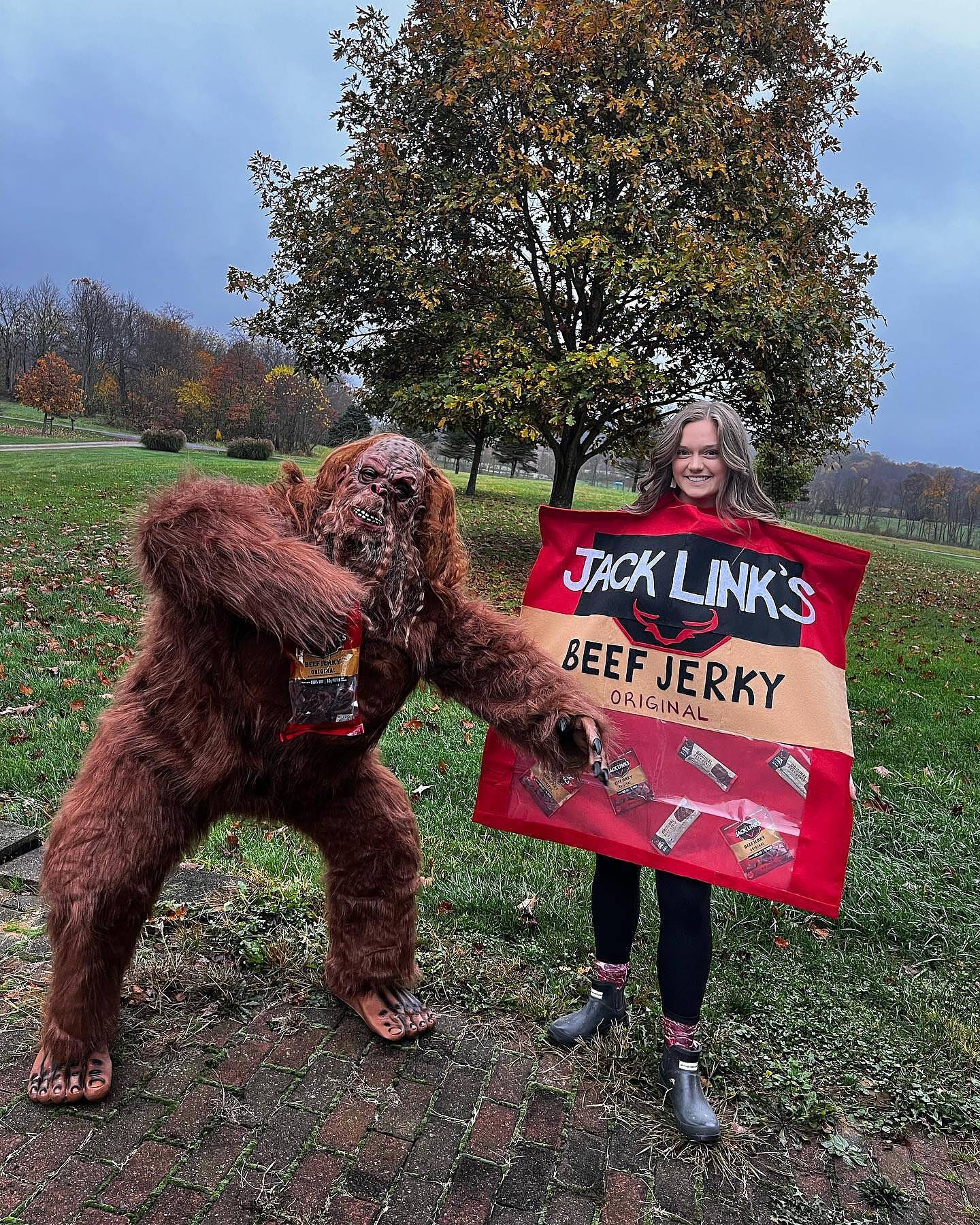 A person in a Sasquatch costume holds a bag of Jack Link’s jerky while point towards a woman dressed as a bag of jerky for Halloween. 