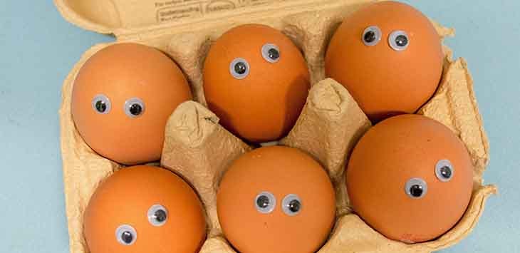 Photo of some eggs in an egg box with little googly eyes attached to each egg.