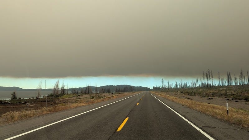 The top half of the photo is solid gray smoke, the bottom half of the photo shows clear sky in the distance over a highway