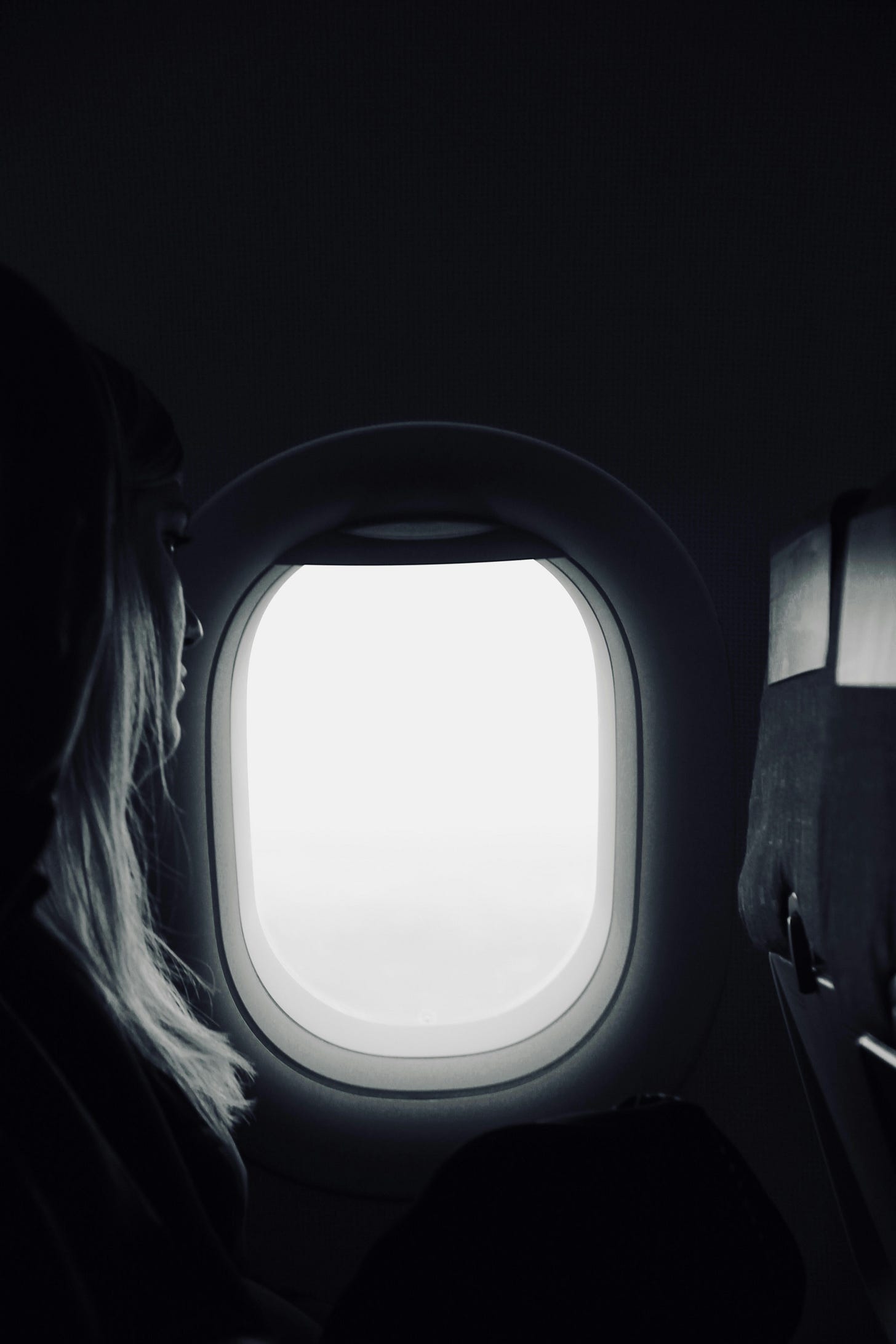 profile of woman with long hair looking out a large, luminous oval window on an airplane