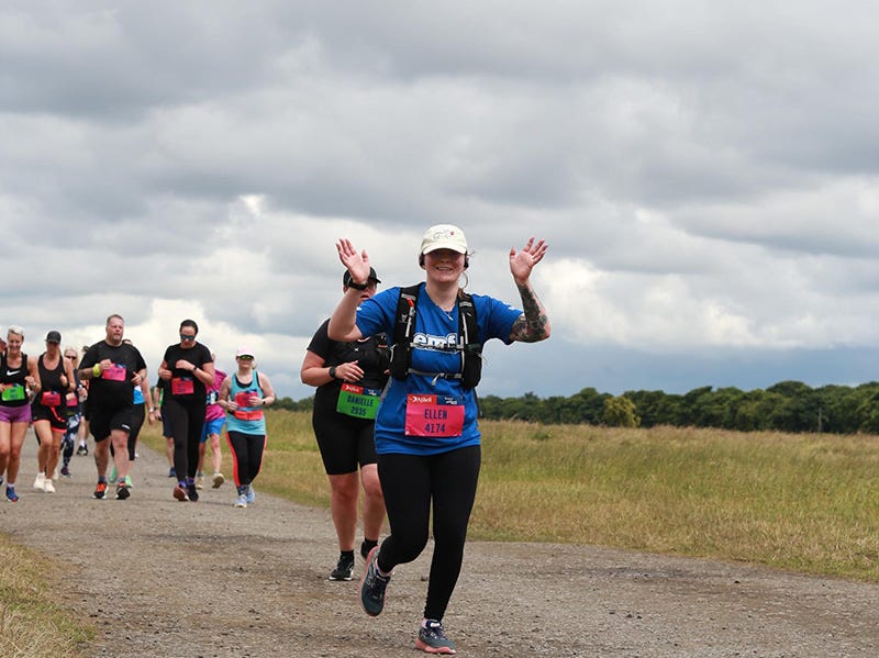 Ellen waving at the camera while running through Newcastle's Town Moor