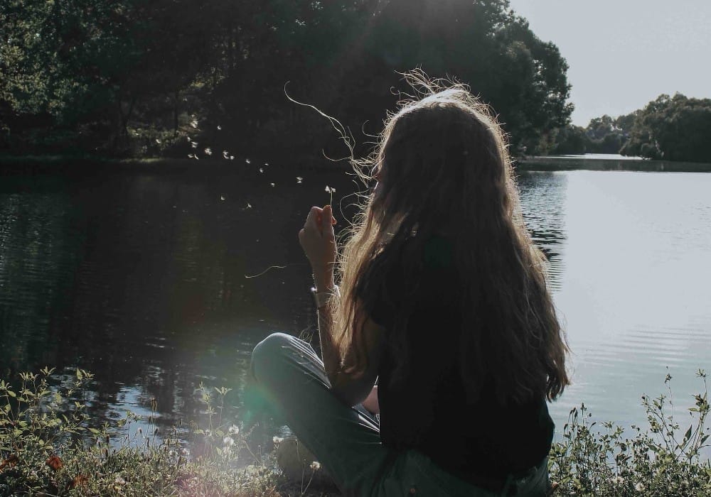 Girl by the lake blowing a dandelion