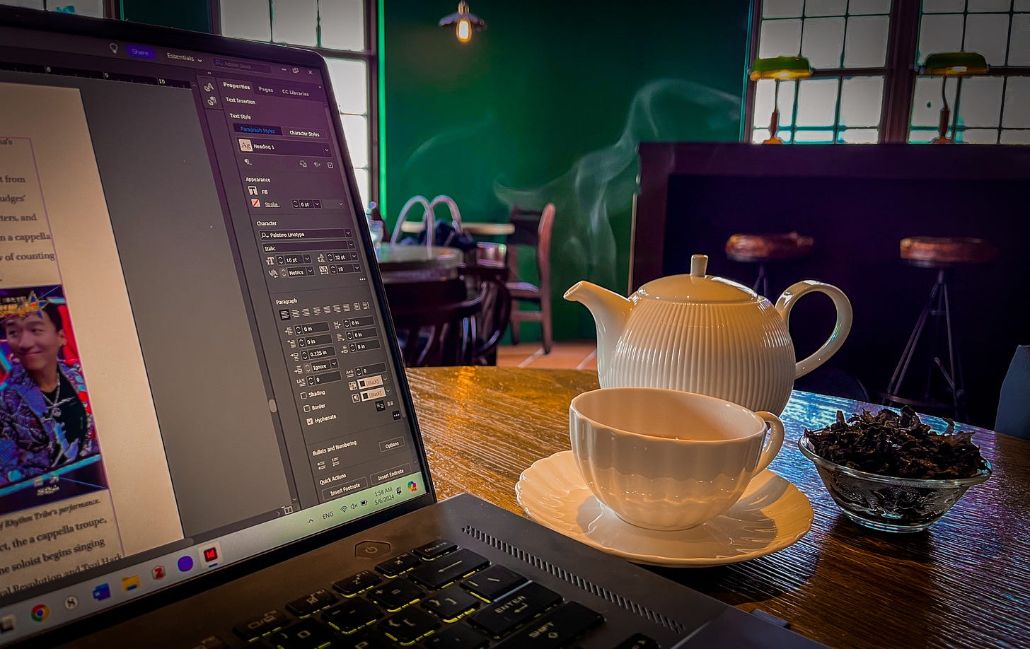 Steam rises over a white ceramic teacup sitting between an open computer, a teapot, and a glass bowl of tea leaves in Taipei's Dadaocheng