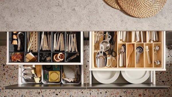 Four pulled-out MAXIMERA kitchen drawers with various items in a cutlery tray, an adjustable organizer for drawer and boxes.