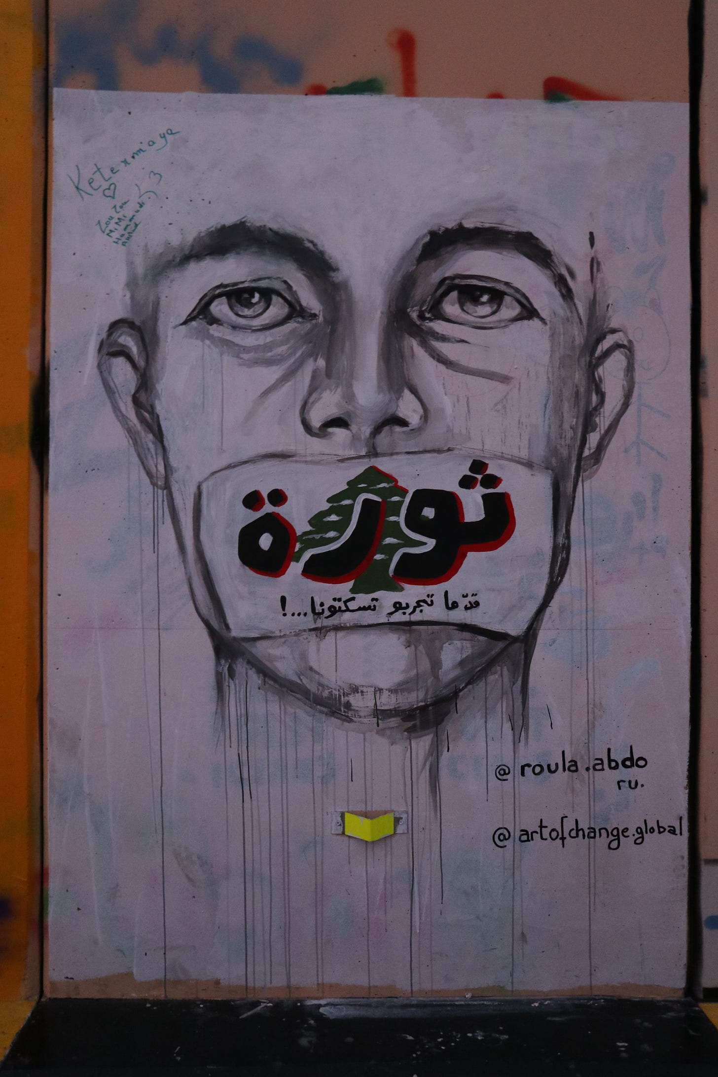 Street art shows a man with a Lebanese flag taped across his mouth, with the Arabic word "thowra" written on the flag.