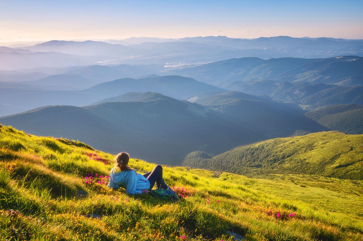 Person Lying in Field Enjoying Majestic Nature and Mountains