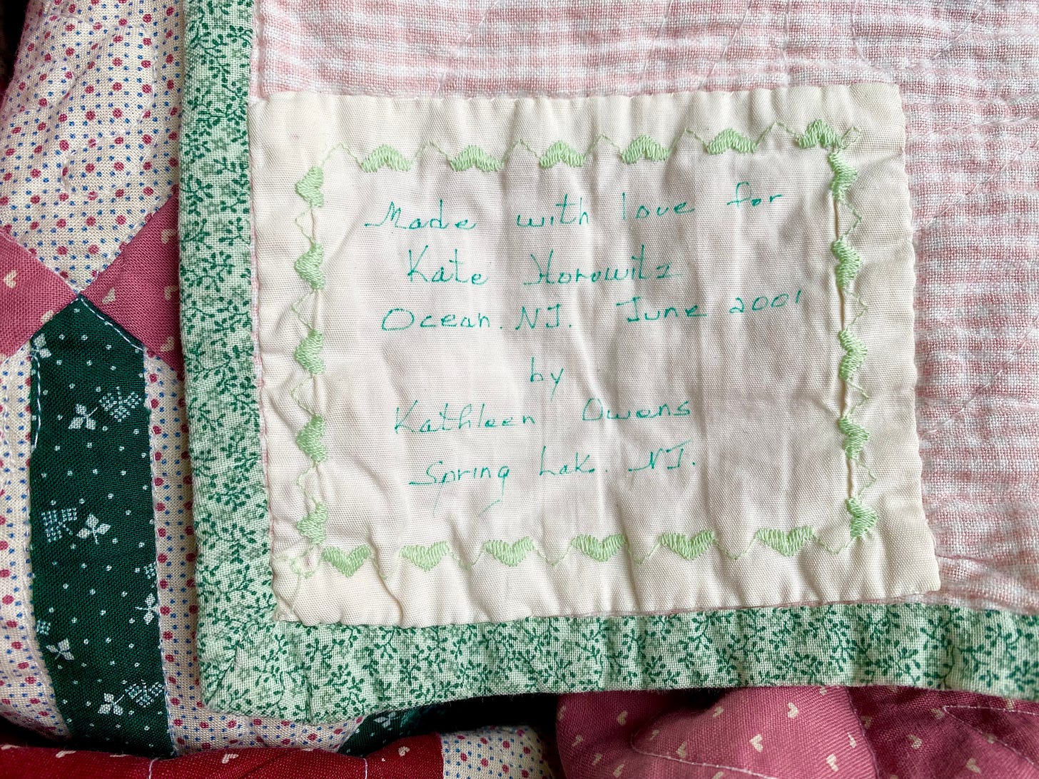 Closeup of a patchwork quilt. The handwritten label says "Made with love. Kate Horowitz, Ocean, NJ. June 2001. by Kathleen Owens, Spring Lake, NJ.