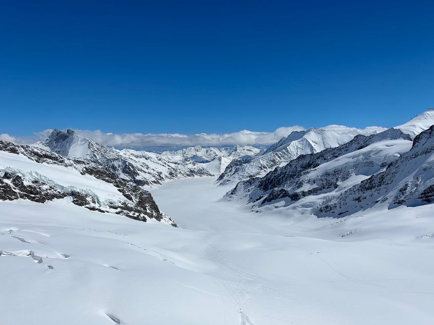 A snow-covered glacier surrounded by mountains, under a clear blue sky