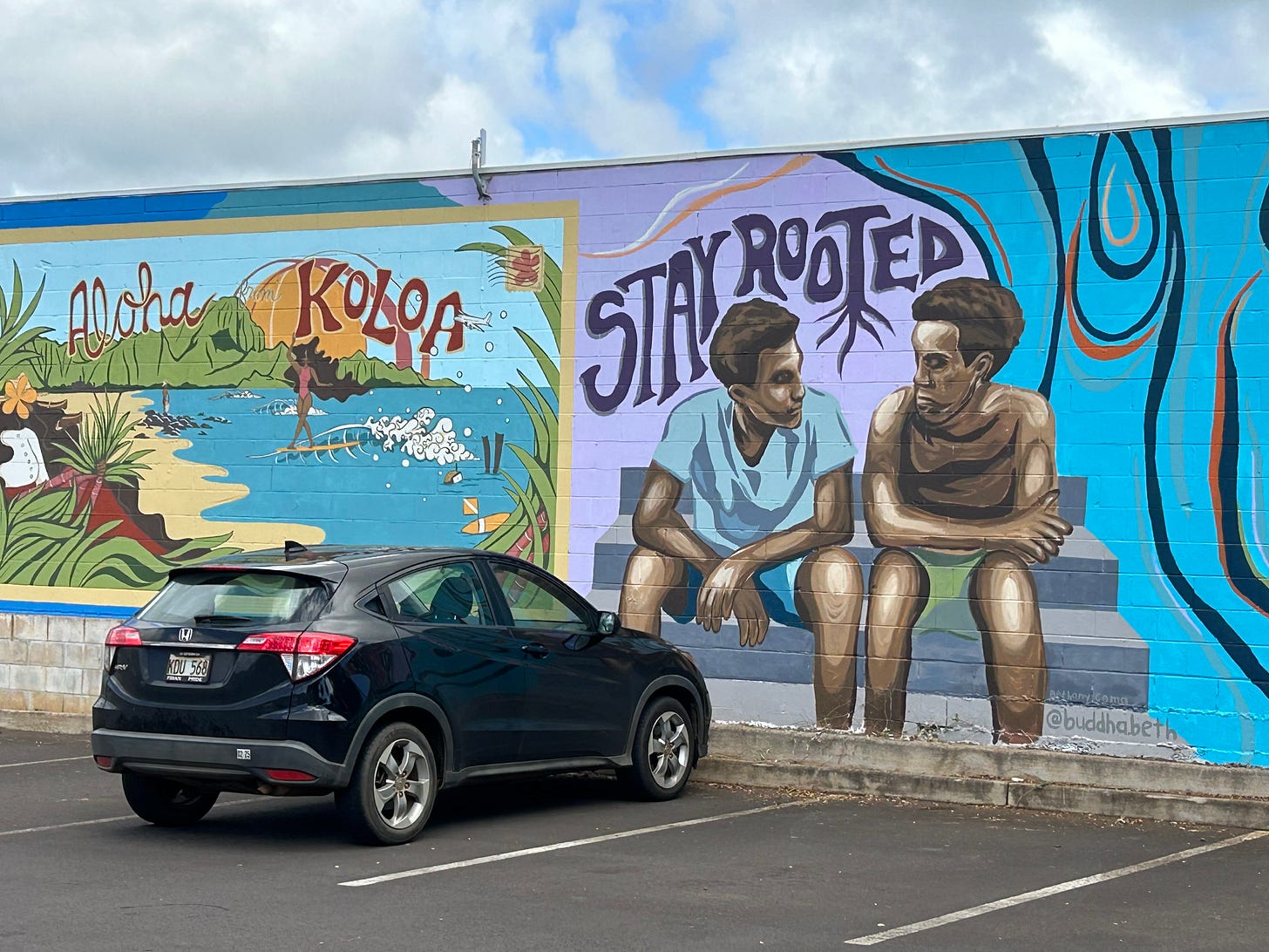 A street mural in Kauai with two kids sitting and looking at each other that says "Stay Rooted" and a Hawaiian beach scene that says "Aloha Koloa"