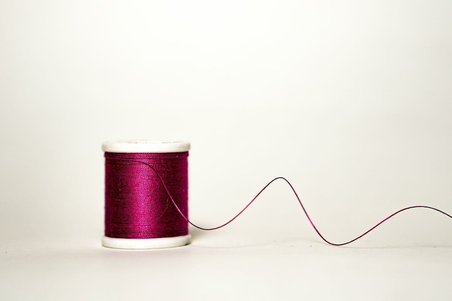 A spool of purple thread with one strand curving off from it.