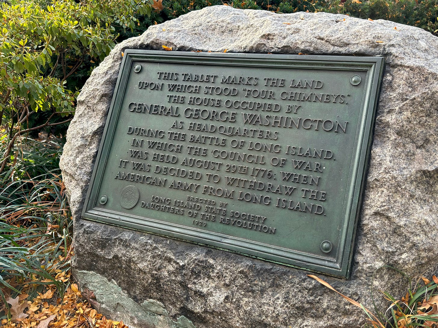 A large rock with a metal plaque embedded in its face. It reads: This tablet marks the land upon which stood “Four Chimneys,” the house occupied by General George Washington as headquarters during the Battle of Long Island, in which the Council of War was held August 29th 1776, when it was decided to withdraw the American Army from Long Island.    Erected 1929 by Long Island State Society Daughters of the Revolution.