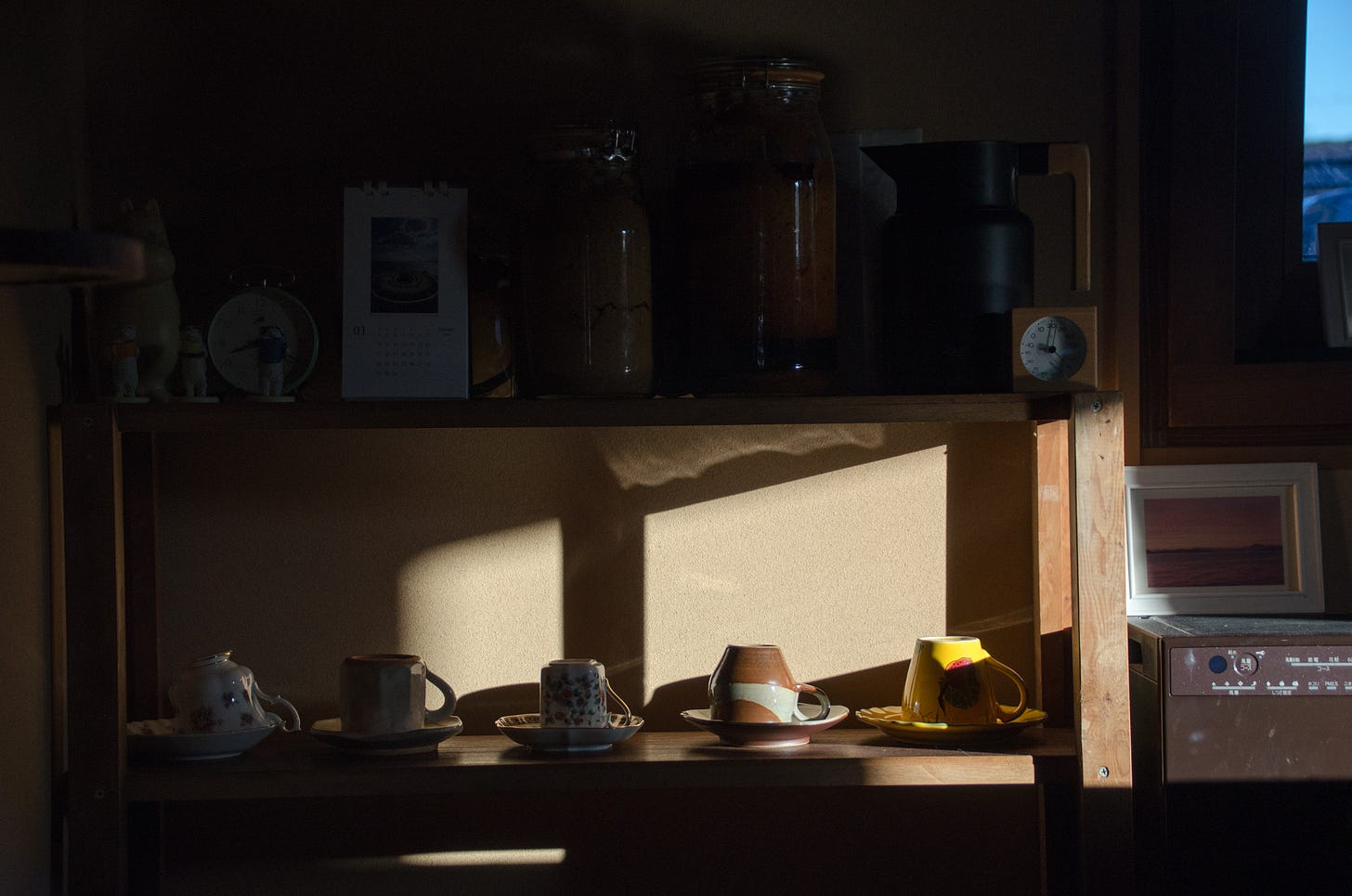 Morning sun against a shelf of mugs, casting a warm shadow