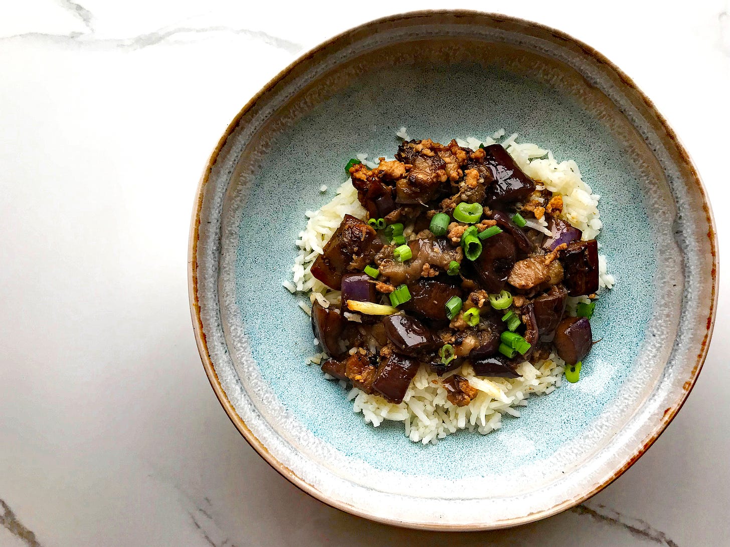 A blue stoneware bowl with rice and wok-fried aubergine with minced pork, topped with sliced green onions.