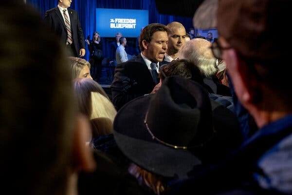 Ron DeSantis stands in the middle of a crowd at book-tour event. A screen far in the background says “The Freedom Blueprint.”