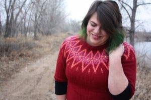 Photo of a woman wearing a handknit sweater in reds and creams. The pattern is Plum Rondo, designed by Julia Farwell-Clay.