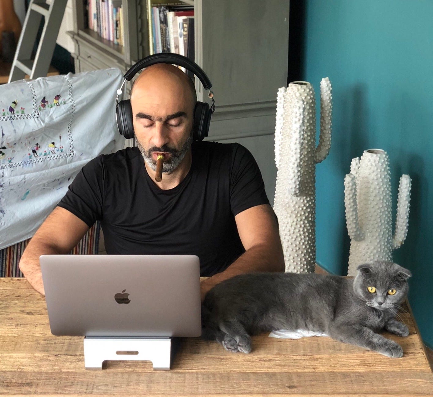 A person wearing headphones and smoking a cigar while sitting at a desk with a cat

Description automatically generated