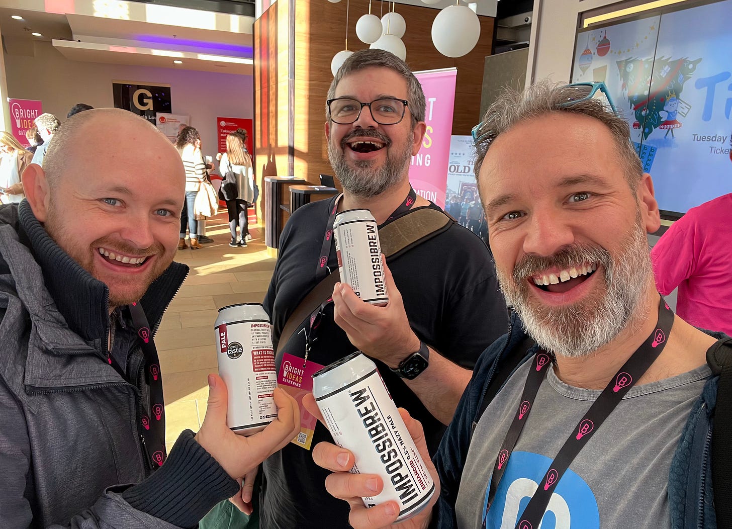 A photo of three white middle aged men with beards holding identical canes of fake beer called Impossibrew. Everyone is smiling.