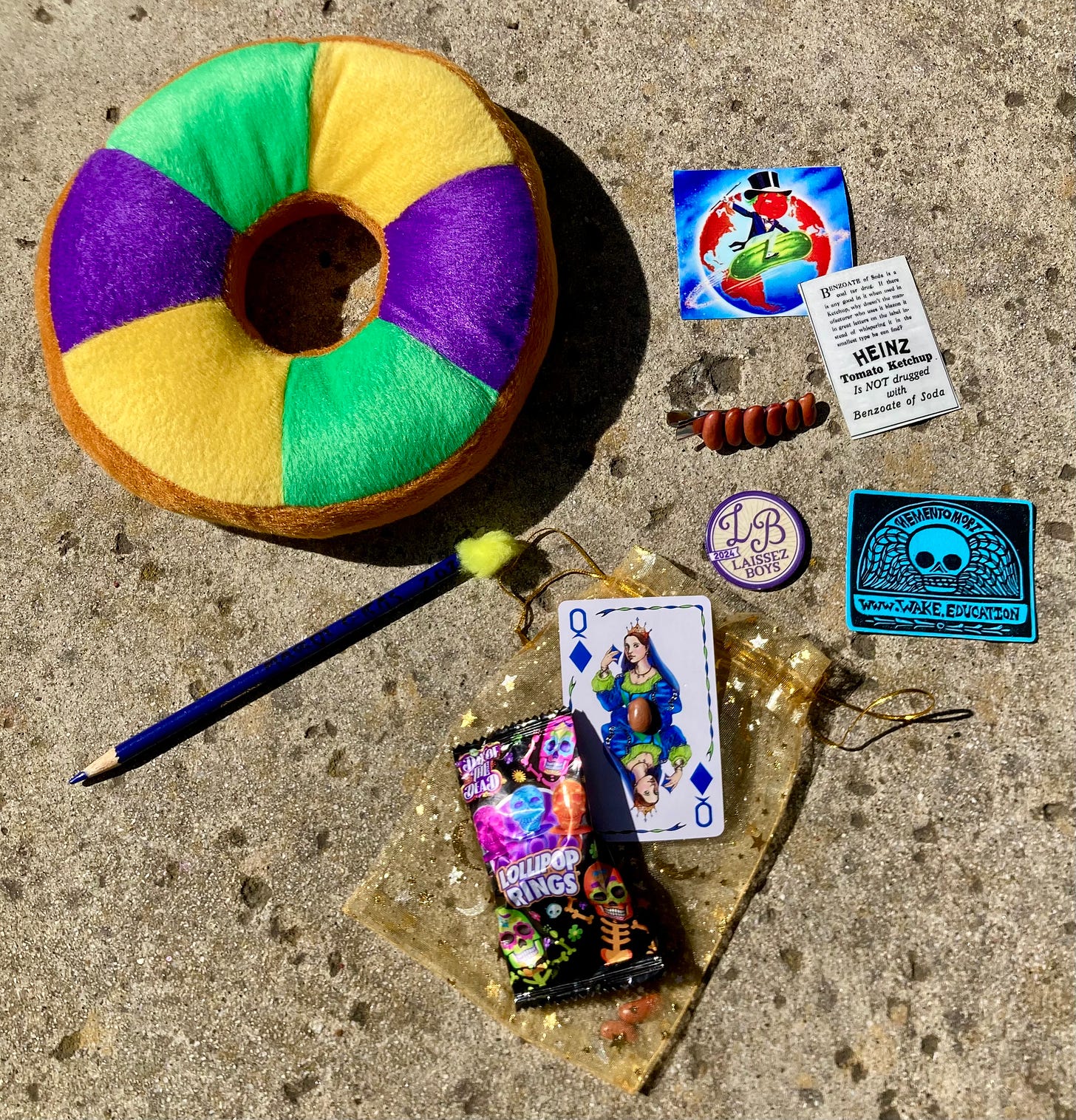 A selection of personalized Mardi Gras throws, including a red beans hair clip, a poker chip, a playing card with a red bean affixed to it, and a memento mori magnet