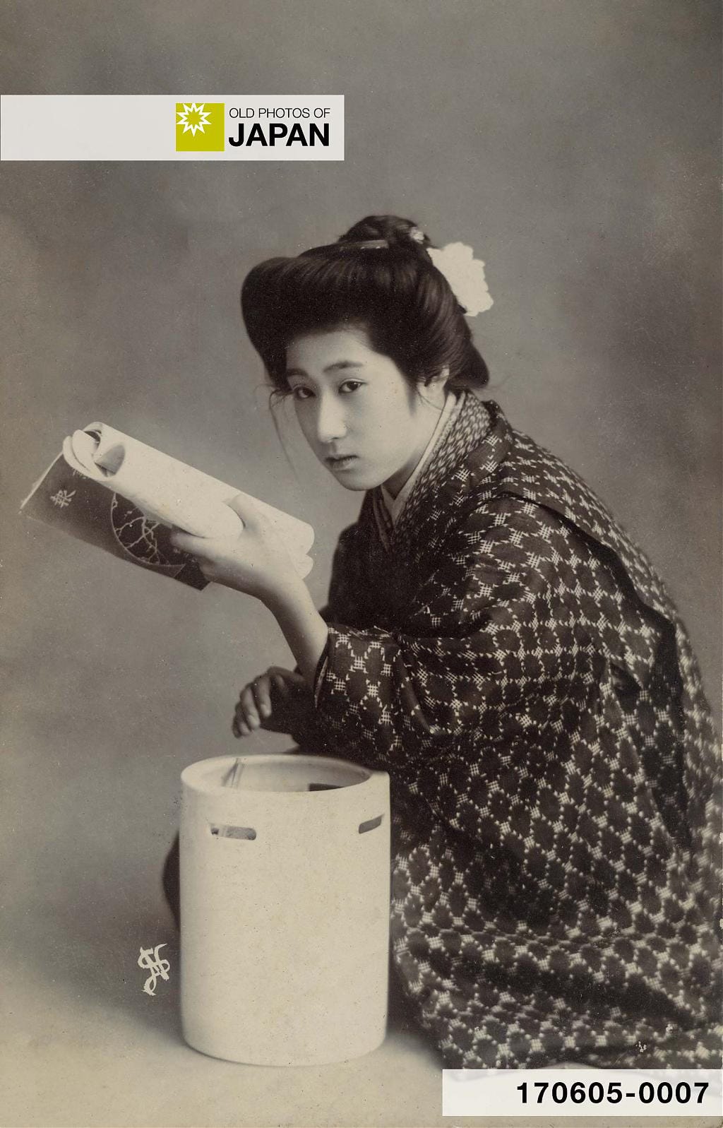 A geisha reading a book while leaning on a hibachi, 1910s A geisha reading a book while leaning on a hibachi, 1910s