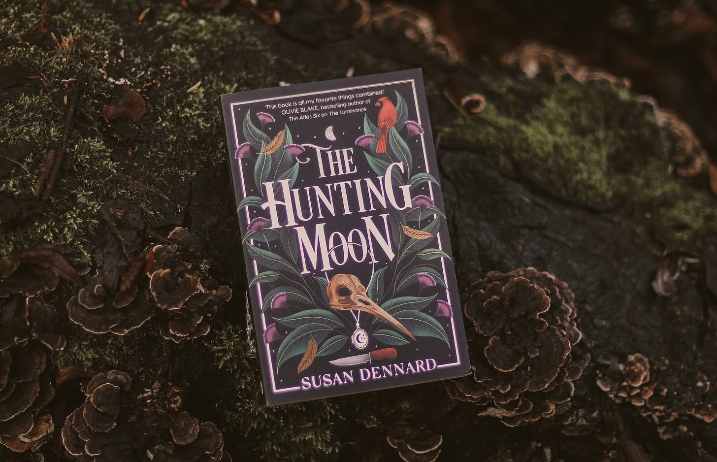 A photograph of the UK edition of The Hunting Moon against a backdrop of moss and wood